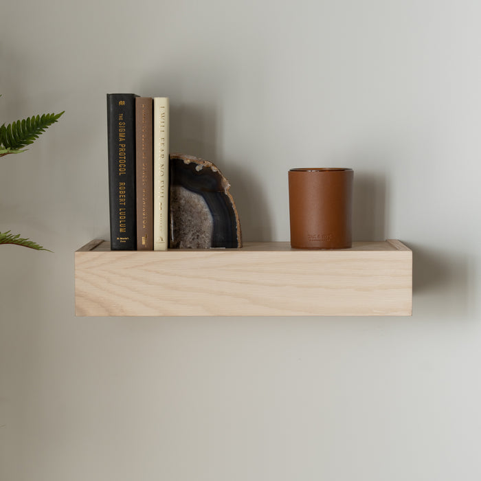 Murphy Door® floating shelf in light wood with books, agate bookend, and brown leather container on minimalist wall display.