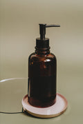 Amber glass soap dispenser with matte black pump on a small round coaster
