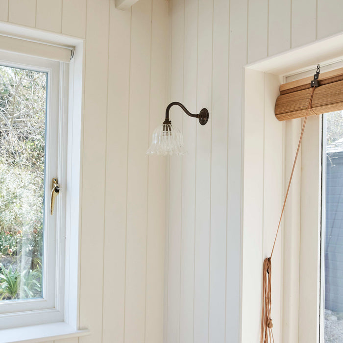 Nook with a wall sconce, window, and yellow flowers on a white paneled wall.