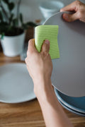 Green ribbed cellulose sponge cloth held against a ceramic plate
