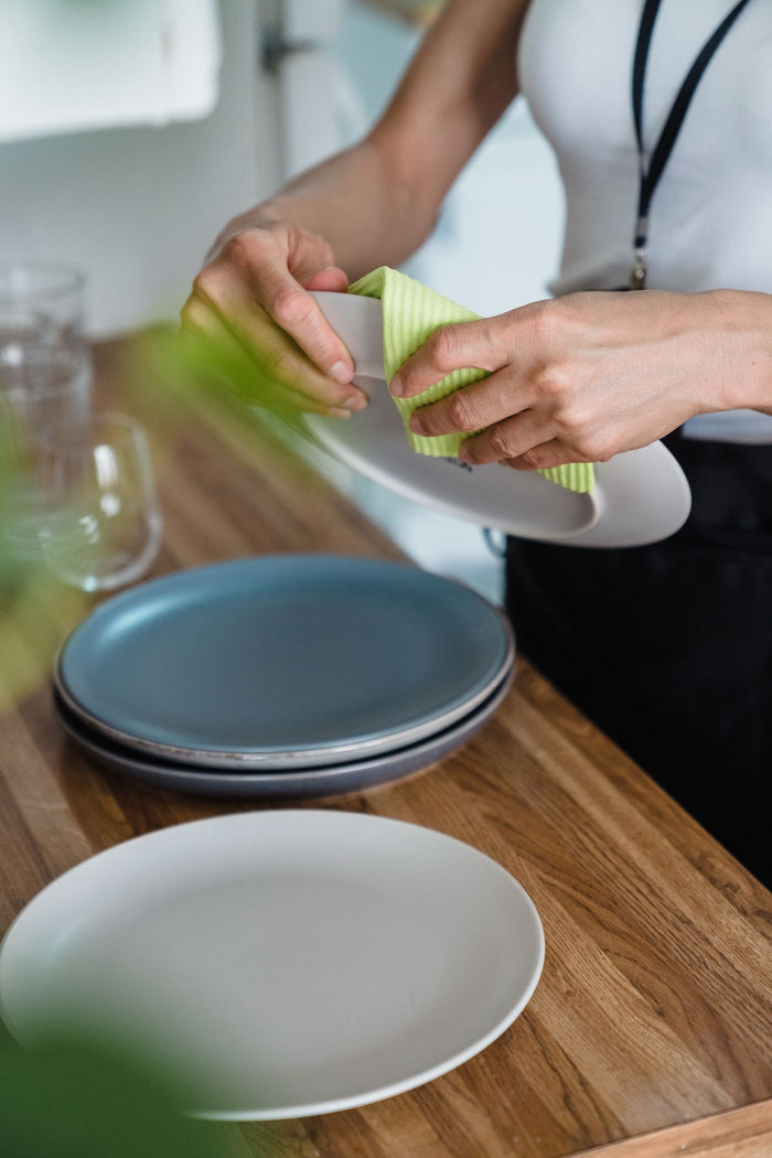 Person wiping a plate with a green cellulose sponge cloth