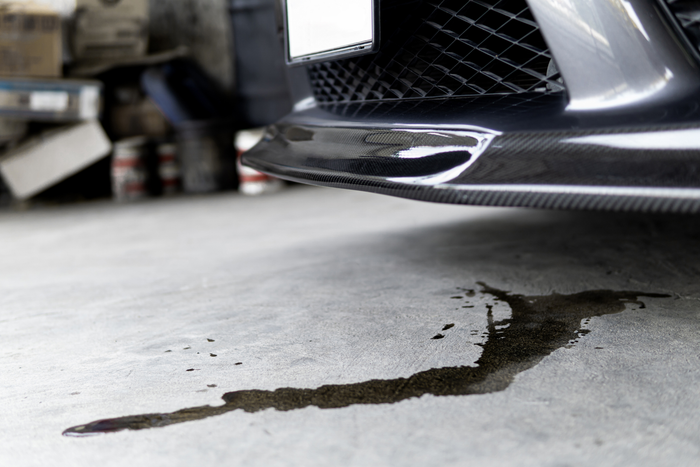 Car oil spill on a concrete floor with a car in the background