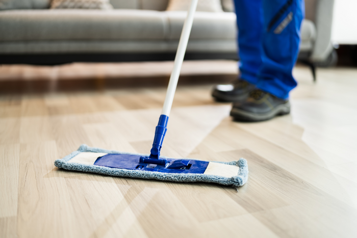 Person cleaning a wooden floor with a flat mop.