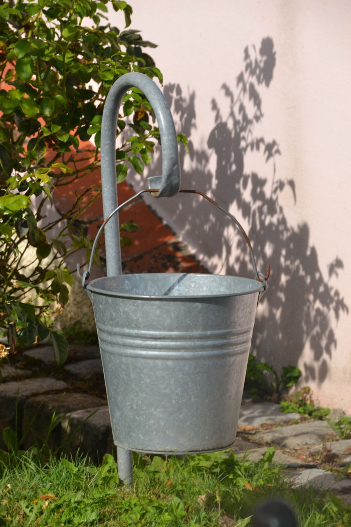 Galvanized metal utility bucket with wire handle hanging in a sunny garden