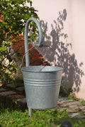 Galvanized metal utility bucket with wire handle hanging in a sunny garden