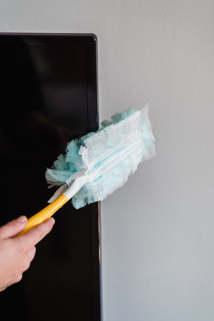 Close-up of a pale blue microfiber duster head on a yellow handle dusting a TV edge