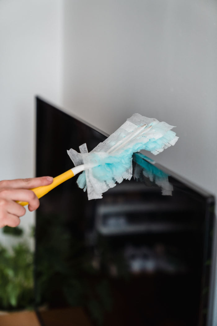 Pale blue microfiber duster on a yellow handle held against a flat screen corner