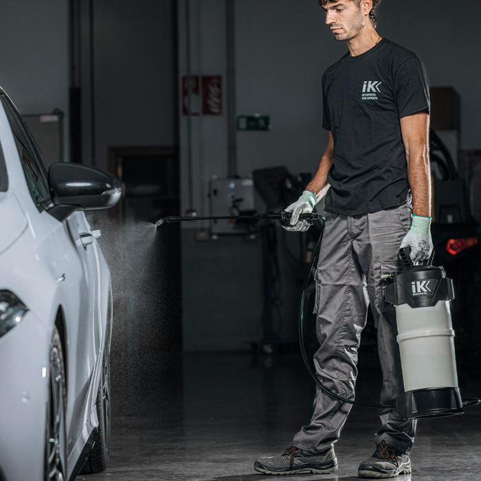 Person in a garage using a car cleaning tool, wearing an IK branded shirt.