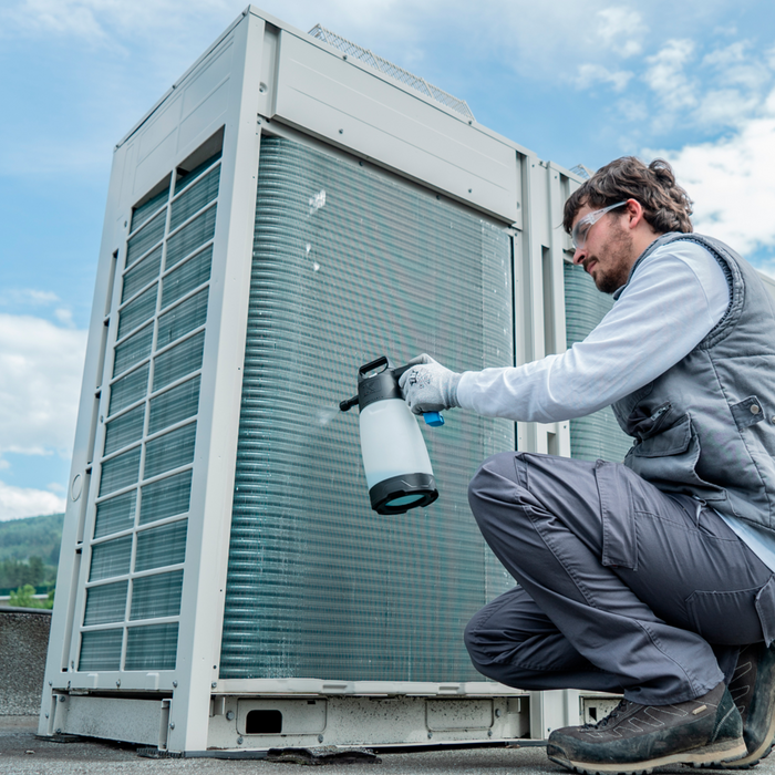 Person servicing an outdoor air conditioning unit with a IK spray bottle.