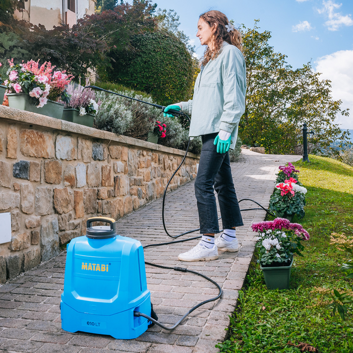 Person using a pressure washer next to a stone wall and potted plants