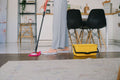 Yellow rectangular mop bucket on a wood floor beside a flat mop with a chenille pad