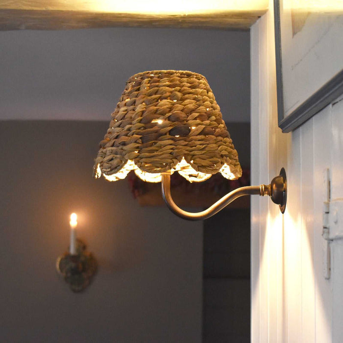 Natural seagrass shade wall light with scalloped edge creating warm, cozy ambience