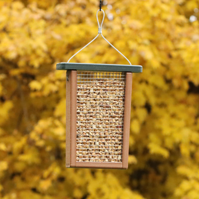 A brown bird feeder with a green top made of recycled plastic and filled with peanuts. Has a wire mesh side. Feeder has a hanging cable.