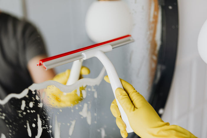 Close-up of a white-handled squeegee with red rubber blade clearing foam from a mirror