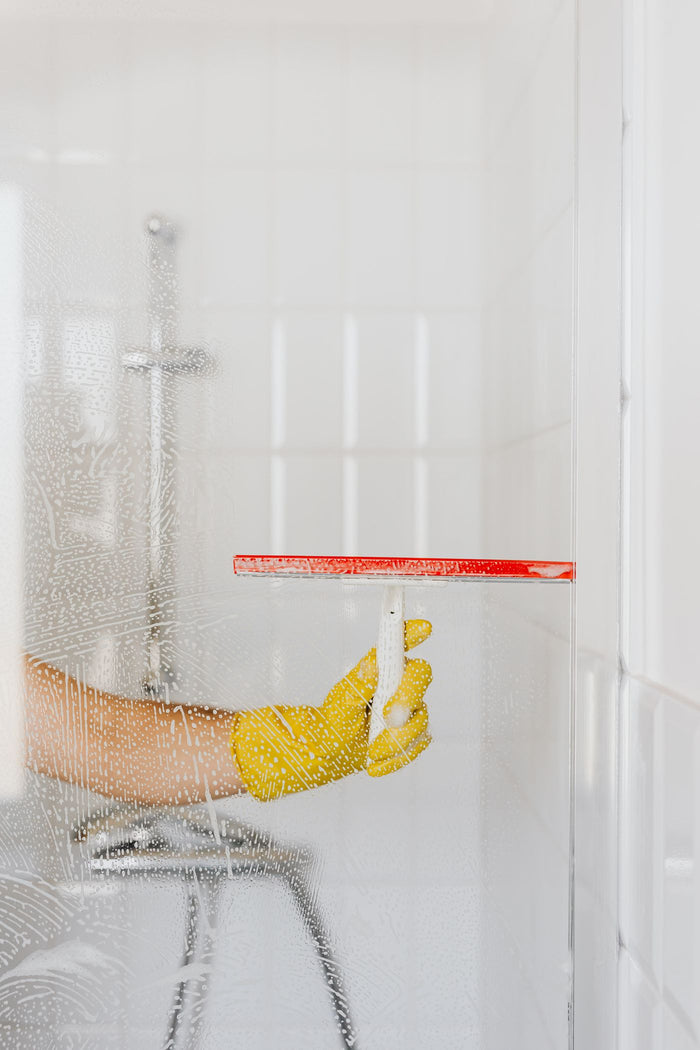Squeegee with red rubber blade clearing water from a glass shower screen