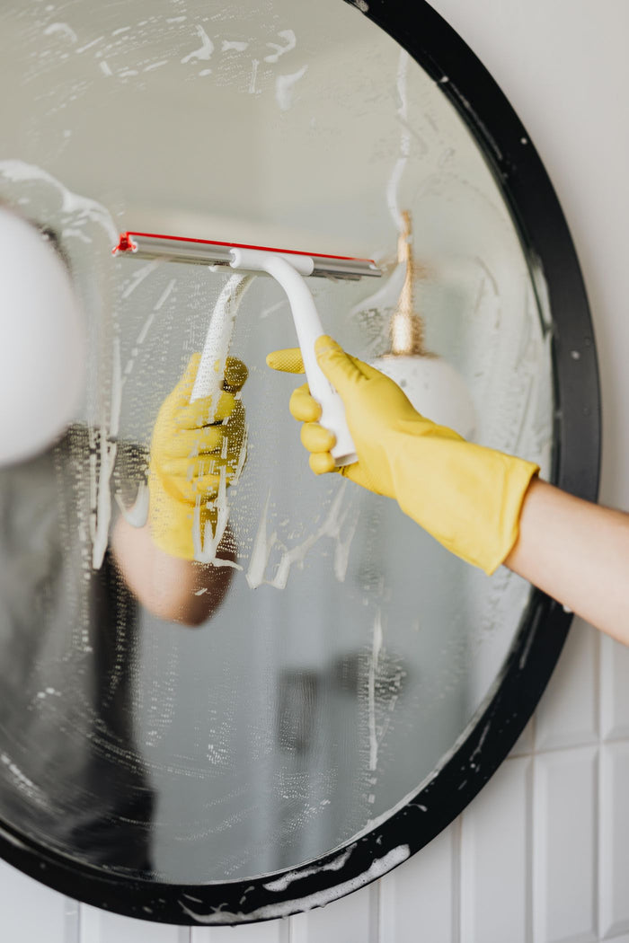 Squeegee pulling foam off a round black-framed bathroom mirror