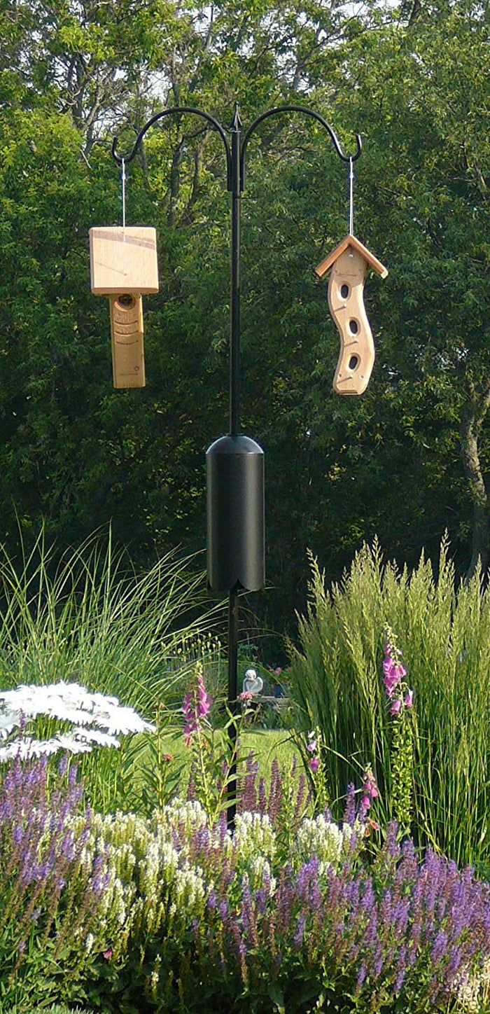 Bird feeders on two arm pole kit with a squirrel baffle. Standing in a garden.