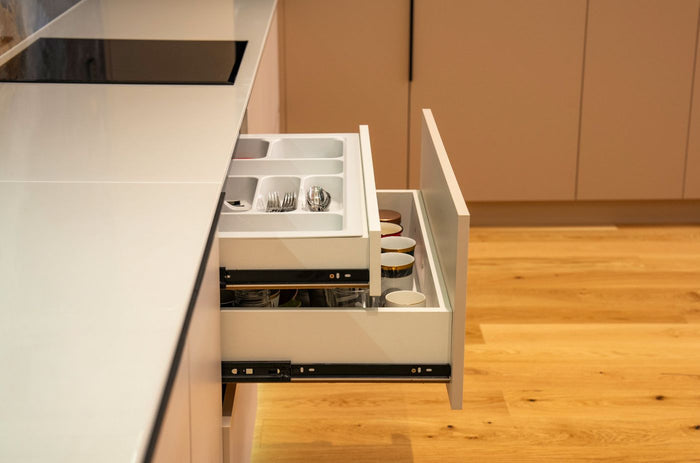 Side view of an open kitchen drawer fitted with a white plastic cutlery tray insert