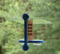 Recycled plastic window mount feeder with 2 suction cups and blue mounting bracket. Has 12 holes on both sides of brown body, a clear acrylic roof, and blue base holds 2 clear cups.