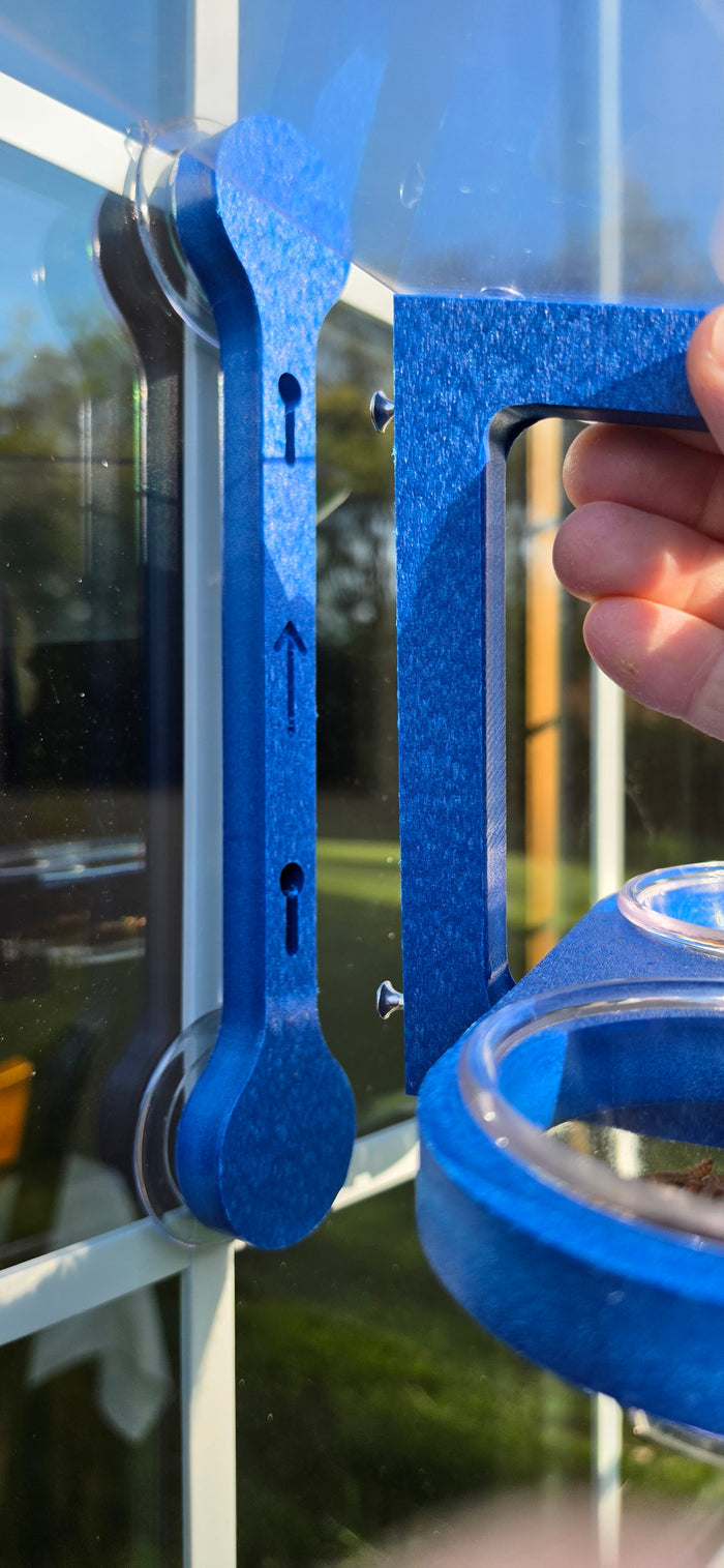 Window bird feeder is detachable from mounting bracket by lifting up. Bracket is secured to the window with two large suction cups. Arrow points up.